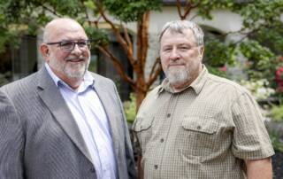 Two smiling men standing outdoors.