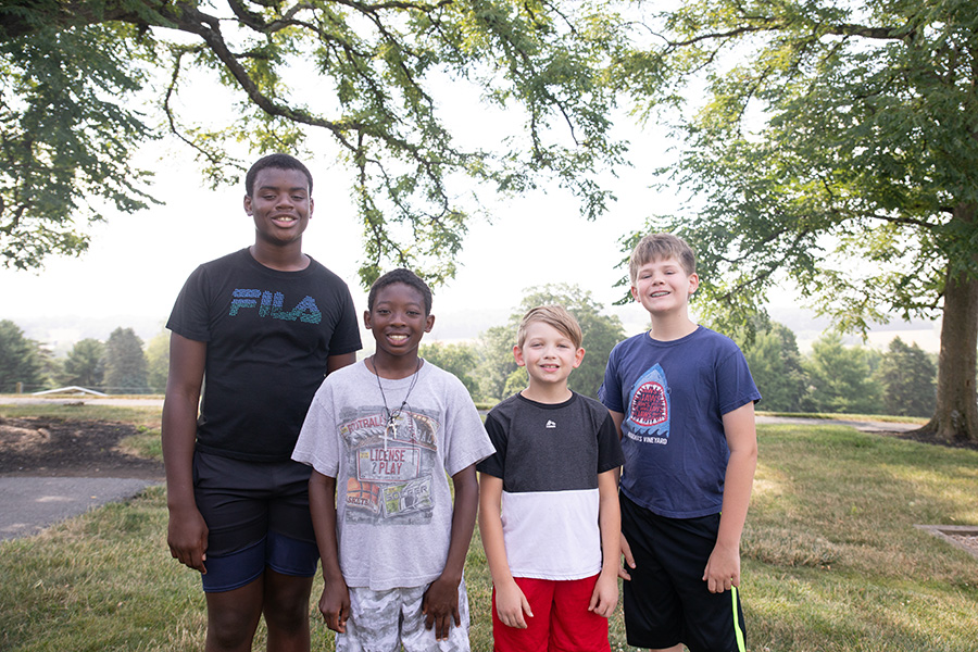 Four smiling boys standing outdoors.